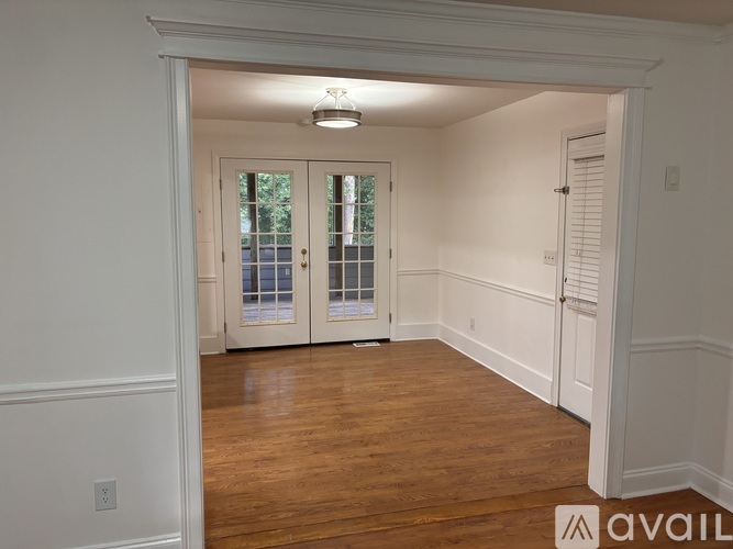 A room with wooden floors and white walls, featuring a large window with a view of trees outside.