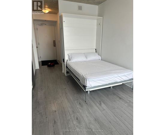 A bedroom with a bed, wooden floor and a white door.