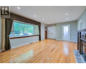 A spacious room with wooden flooring and a large window with curtains.