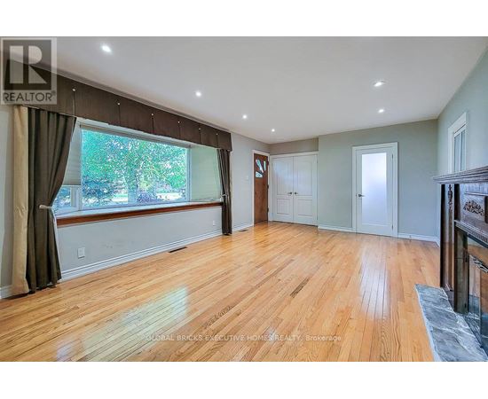 A spacious room with wooden flooring and a large window with curtains.