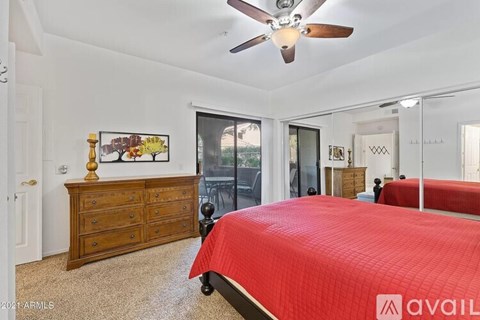 A bedroom with a red bedspread and a ceiling fan.