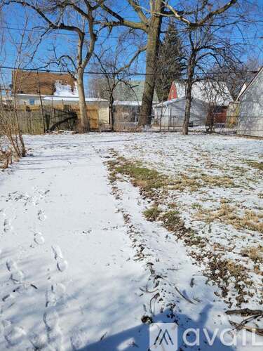 A snowy field with trees and houses in the background.