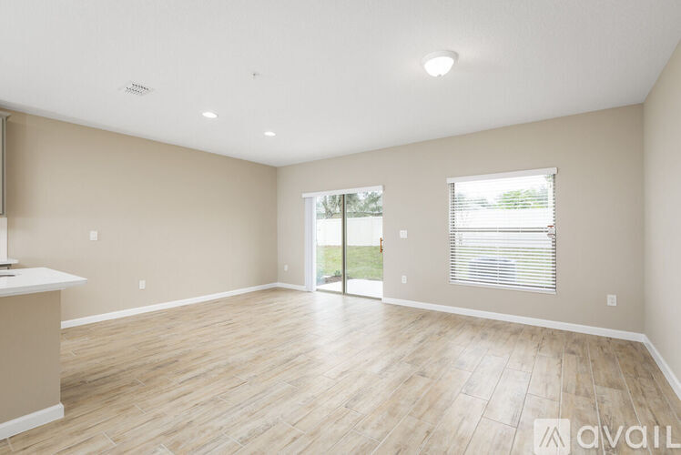 A spacious room with wooden flooring and a large window with blinds.