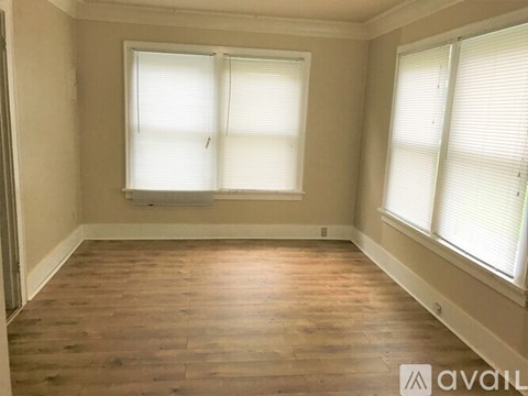 A room with wooden flooring and two windows.