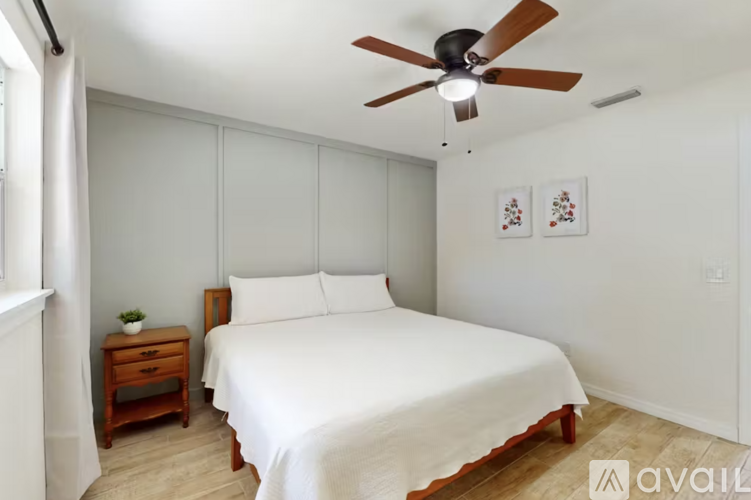 A bedroom with a bed, a ceiling fan, and two pictures on the wall.