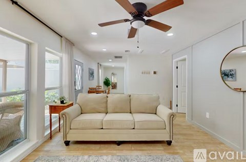 A living room with a beige couch and a ceiling fan.