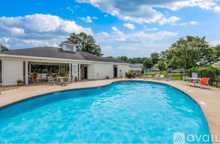 A large swimming pool in front of a house with a patio and chairs.
