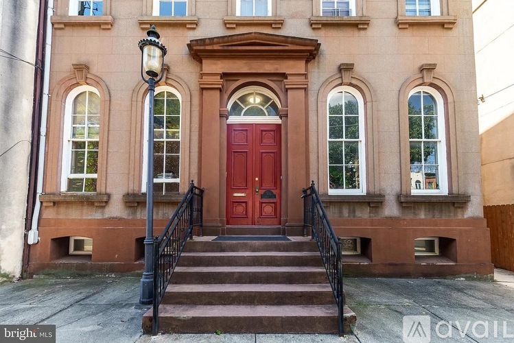 A red door is flanked by two windows on a brick building.
