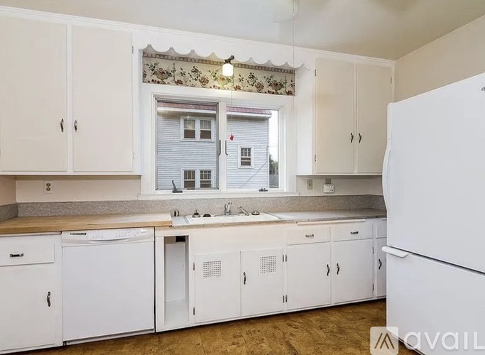 A kitchen with white cabinets and a window with blinds.