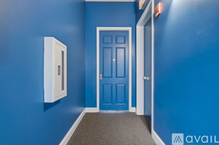 A blue door is in a room with a white wall and a white box on the wall.