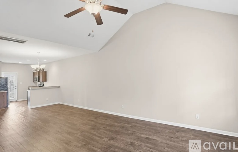 A spacious room with a ceiling fan and light fixture, and a wooden floor.