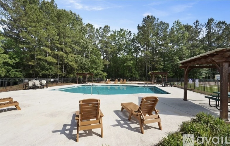 A pool surrounded by trees and wooden chairs.