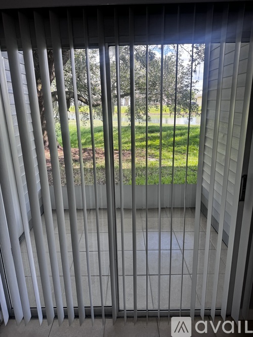 A view through a window with blinds looking out to a green lawn.
