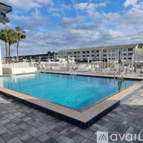 A large swimming pool surrounded by a tiled floor and a white building in the background.