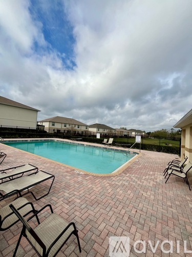 A pool surrounded by chairs and tables with a cloudy sky in the background.