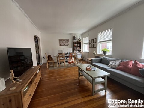 A living room with a grey couch, wooden floors, and a television.
