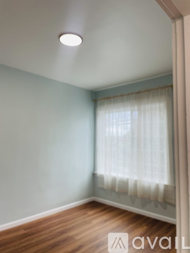 A room with wooden flooring and a window with a view of trees.
