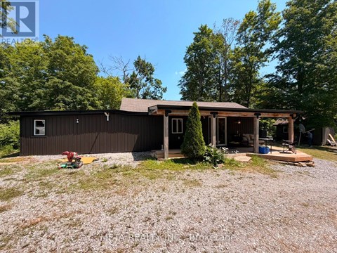 A house with a brown roof and a porch is surrounded by trees.