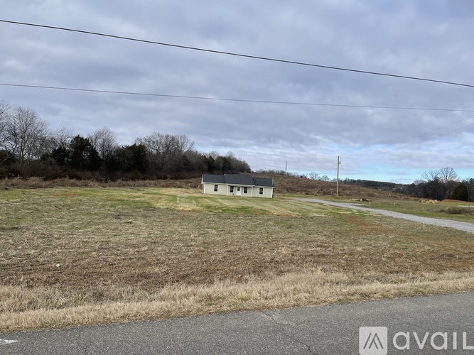 A small white house sits in a grassy field with a road in front of it.