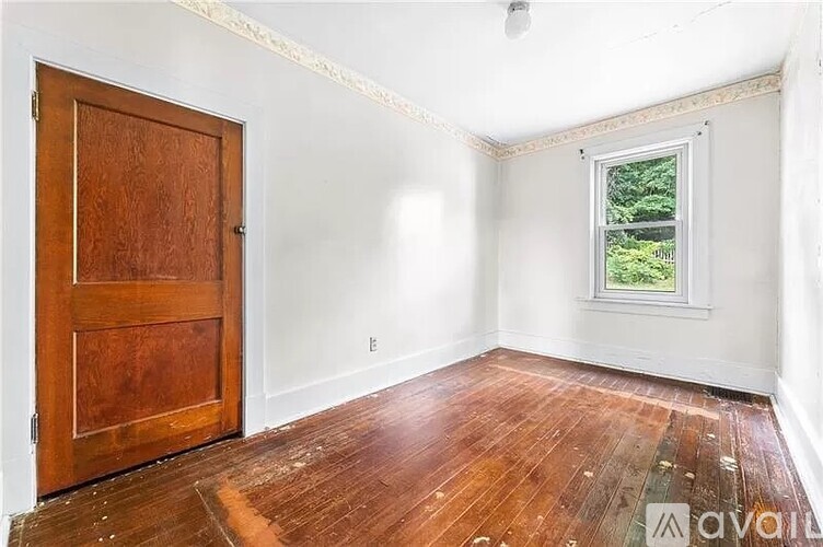 A room with a wooden door and a window with a view of trees outside.