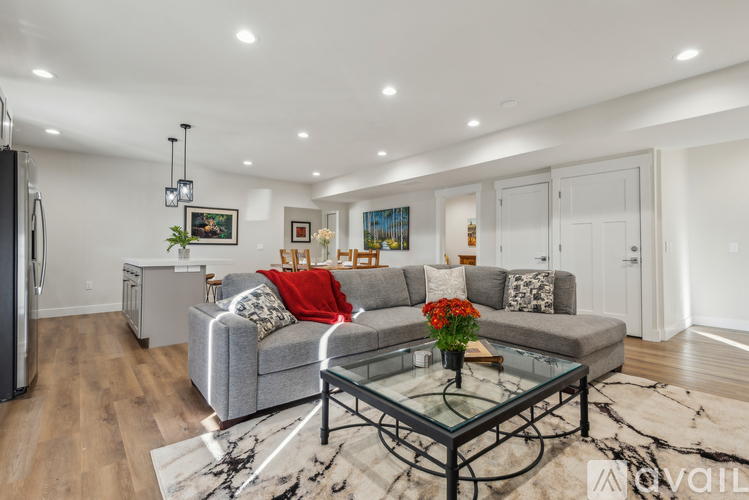 A modern living room with a grey couch, a glass coffee table, and a fridge on the left side.