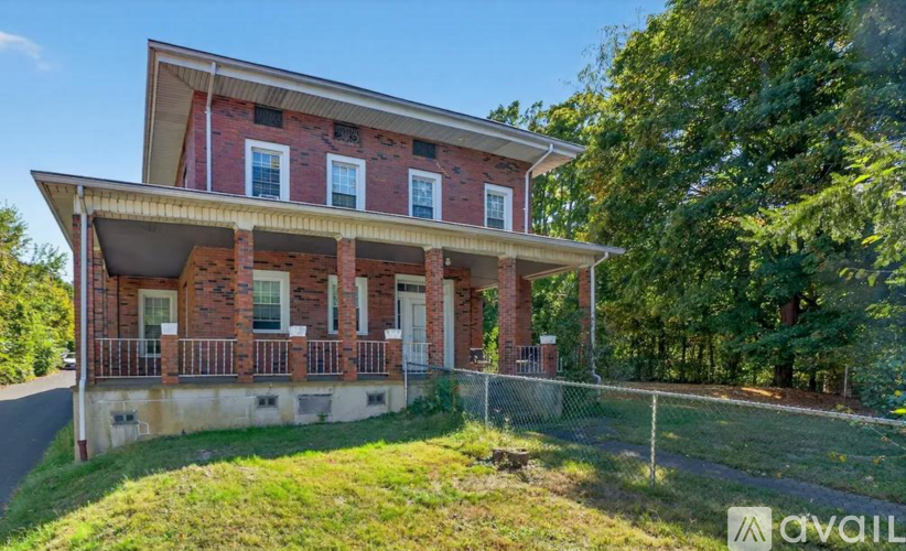 A red brick house with a porch and a fence in front of it.