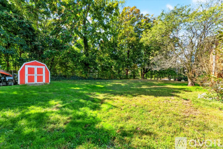 A red barn sits in a field with trees in the background.