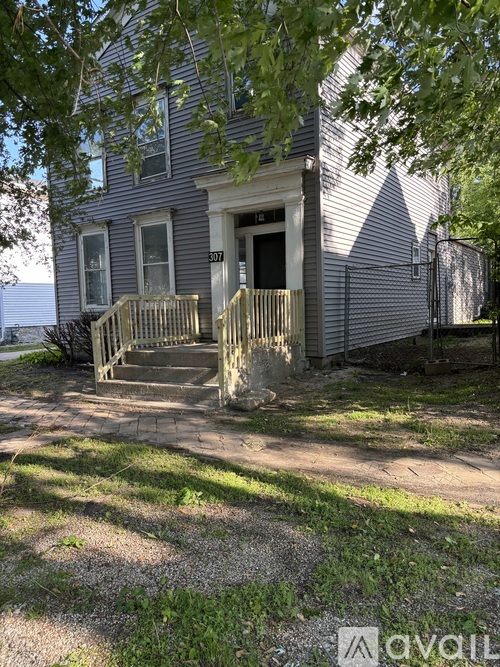 A house with a porch and a tree in front.