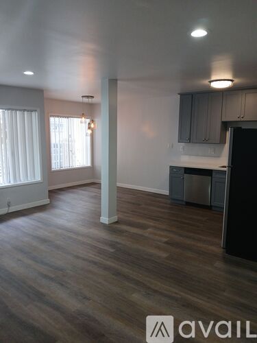 A room with wooden flooring and a kitchen area with a dishwasher.