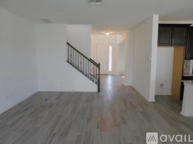 A spacious room with wooden flooring and a staircase with a black railing.