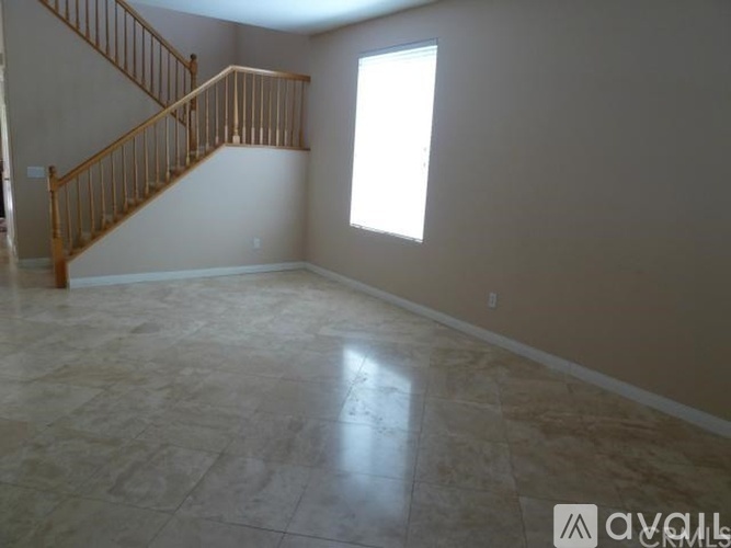 A spacious room with a marble floor and a wooden staircase.