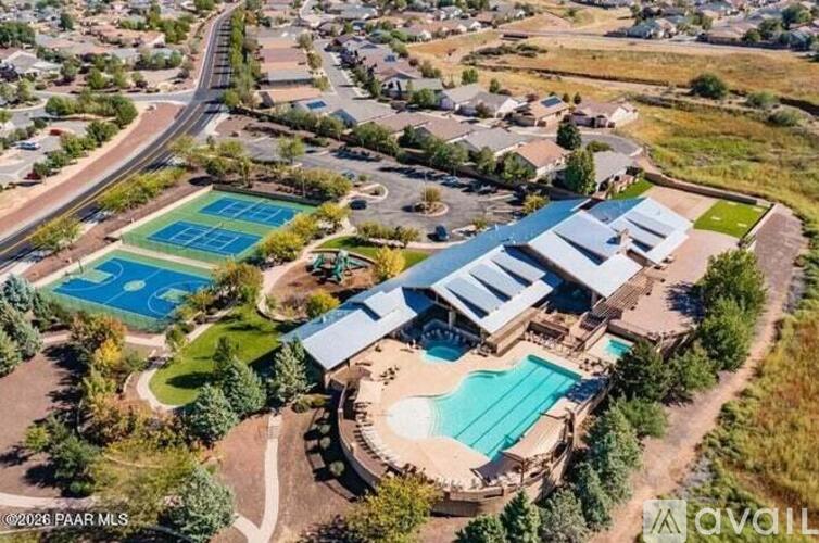 A large outdoor swimming pool and tennis courts are surrounded by a grassy area and a building.