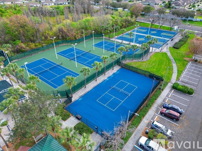 An aerial view of a tennis court surrounded by trees and a parking lot.