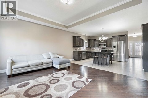 A well-lit, spacious living room with a white sofa and a kitchen area in the background.