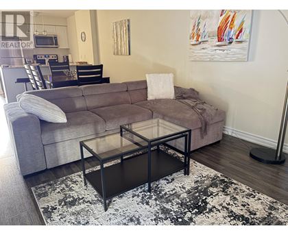 A grey couch with a white pillow and a glass table in front of it.