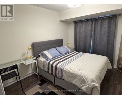 A bedroom with a bed, nightstand, chair, and window with curtains.