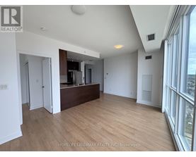 A spacious room with wooden flooring and a large window on the right side.