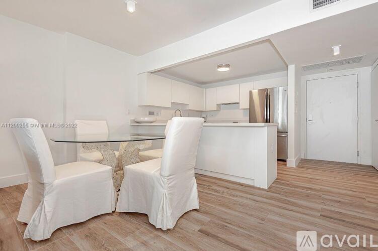 A modern kitchen with white chairs and a glass table.