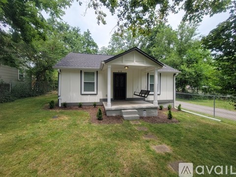 A small house with a front porch is surrounded by a green lawn and trees.