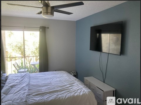 A bedroom with a bed, a ceiling fan, and a window with curtains.