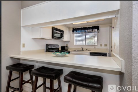A kitchen with white countertops and black bar stools.