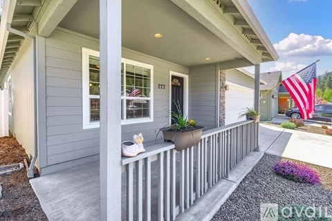 A house numbered 227 has a grey porch with a white railing and a small American flag.