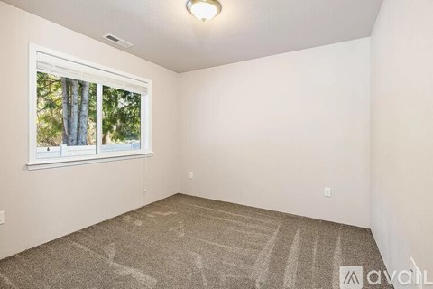 A room with a carpeted floor and a window showing trees outside.