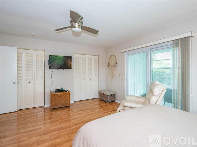 A bedroom with a bed, a chair, a ceiling fan, and a television.