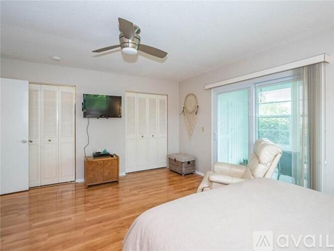 A bedroom with a bed, a chair, a ceiling fan, and a television.