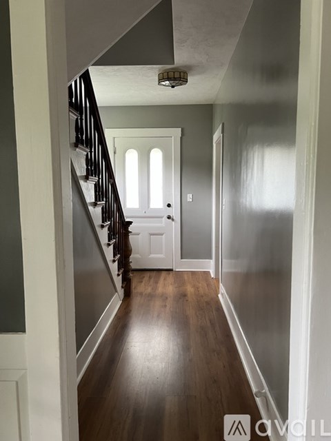 A hallway with a wooden floor and a staircase with a black railing.