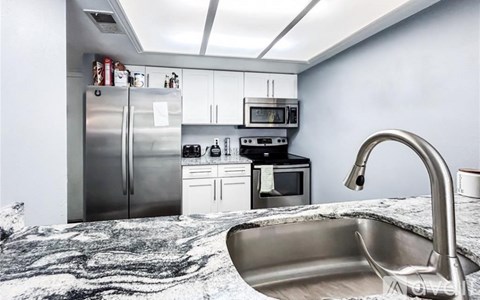 A kitchen with a refrigerator, microwave, oven, and sink.
