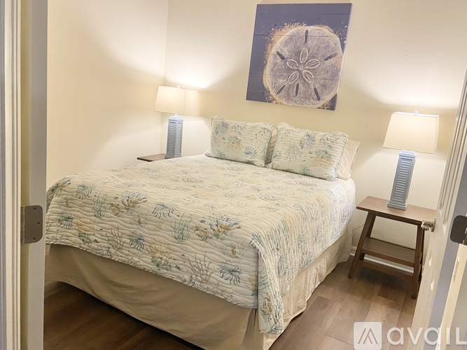 A bedroom with a bed, two lamps, and a painting on the wall.