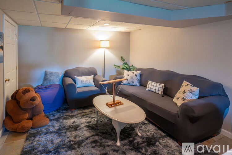 A living room with a grey couch, a blue chair, a brown teddy bear, and a white coffee table.