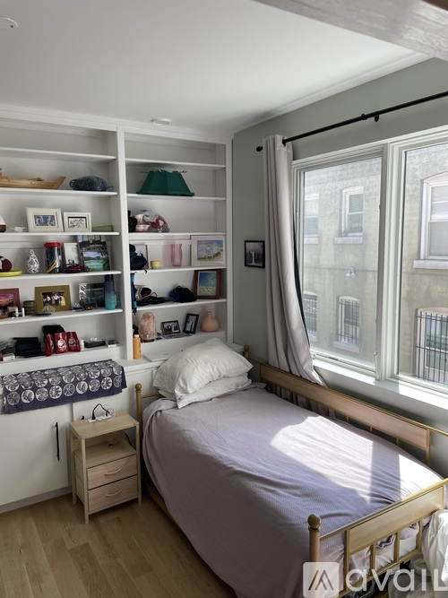 A bedroom with a bed, nightstand, and shelves with various items.